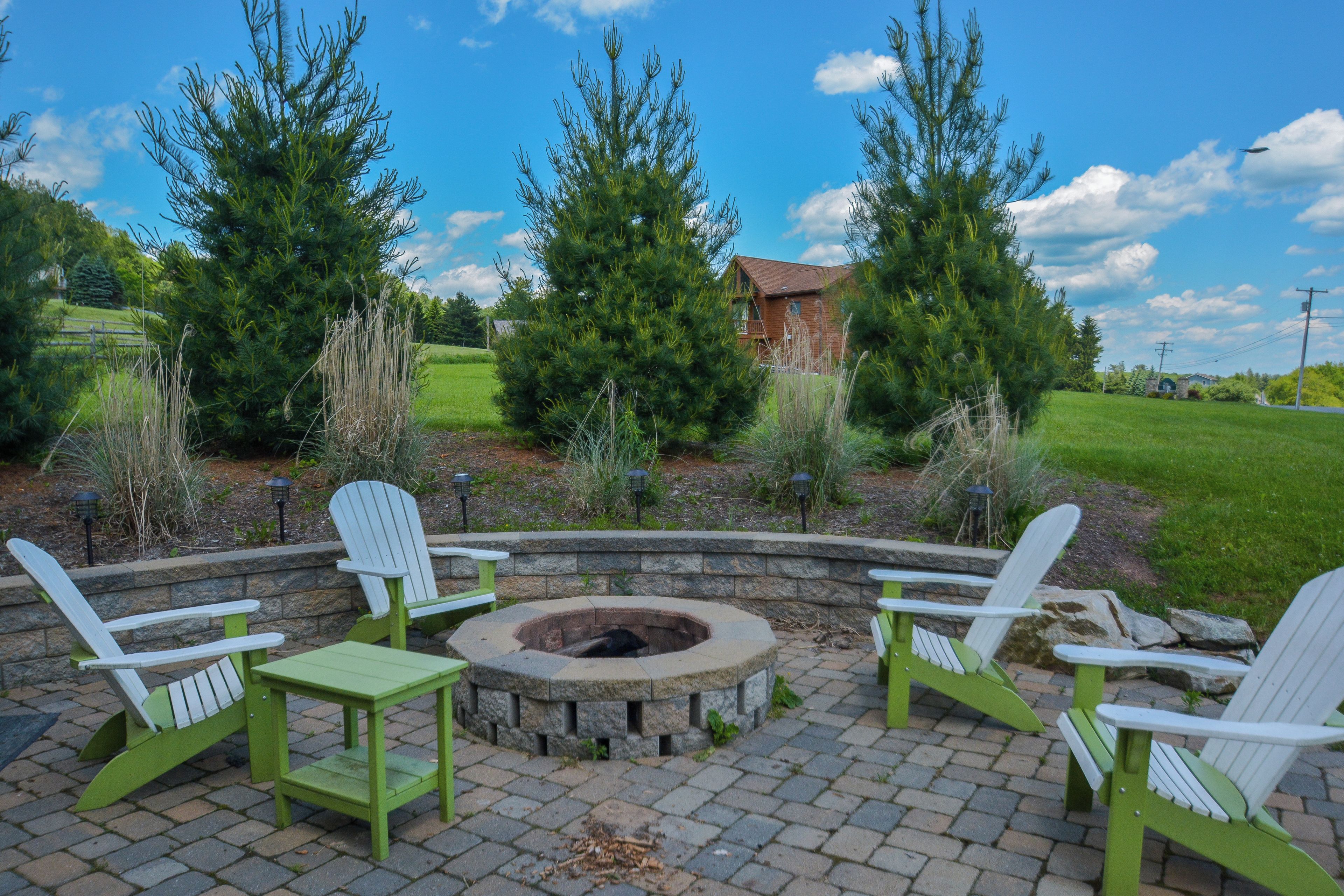 A fire pit surrounded by green Adirondack chairs on a brick patio.
