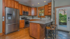 A modern kitchen with wooden cabinets, stainless steel appliances, and a large island with bar stools. - Wine Down by Taylor Made Deep Creek (Oakland)