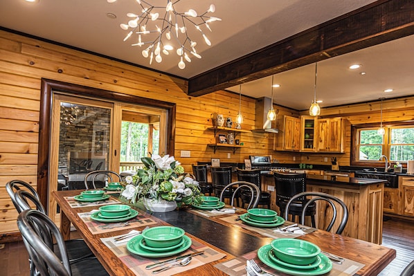 A wooden cabin interior with a dining area, kitchen, and large windows.
