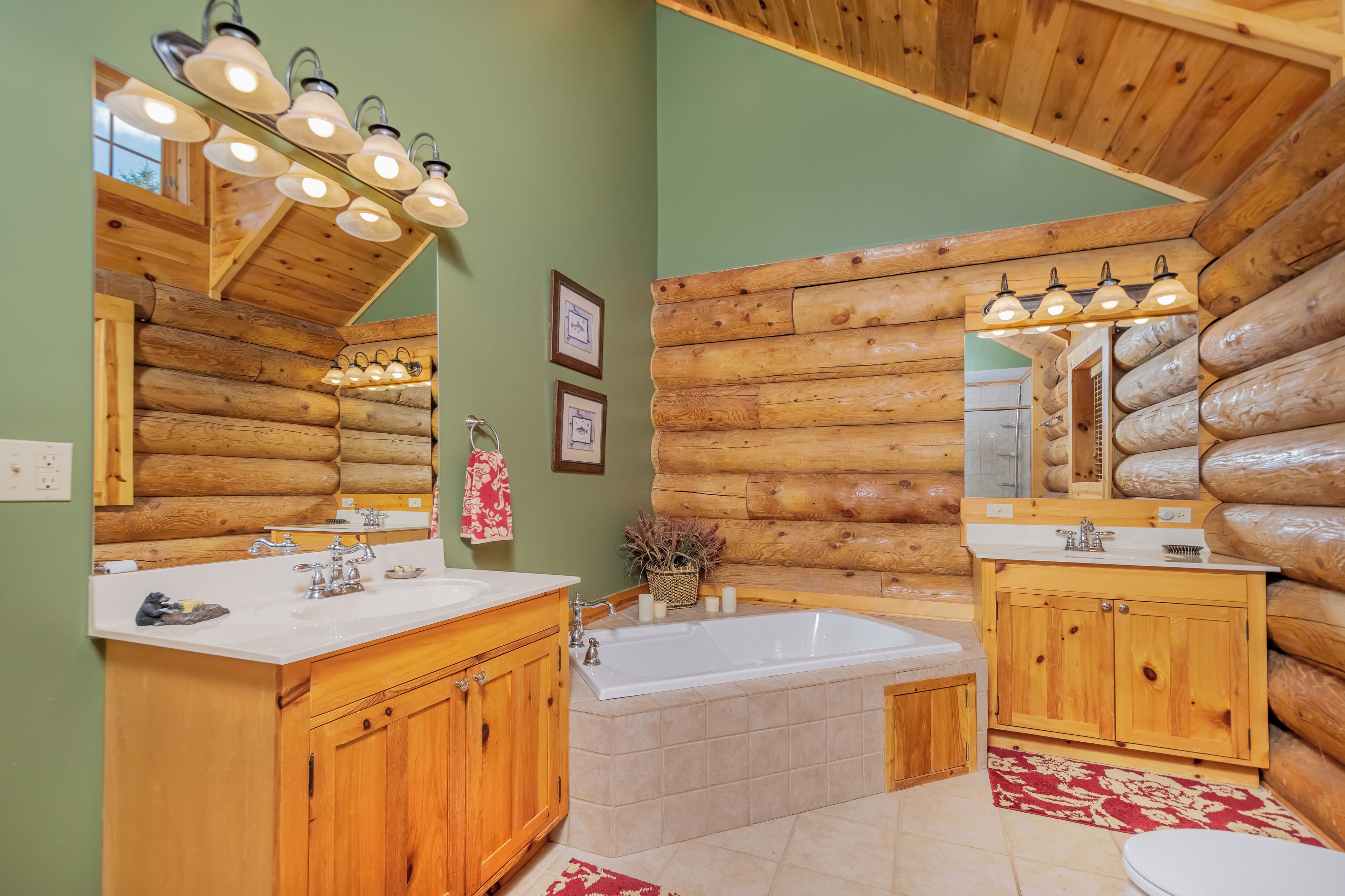 A log cabin bathroom with wooden cabinets, a white sink, a bathtub, and a mirror with lights.