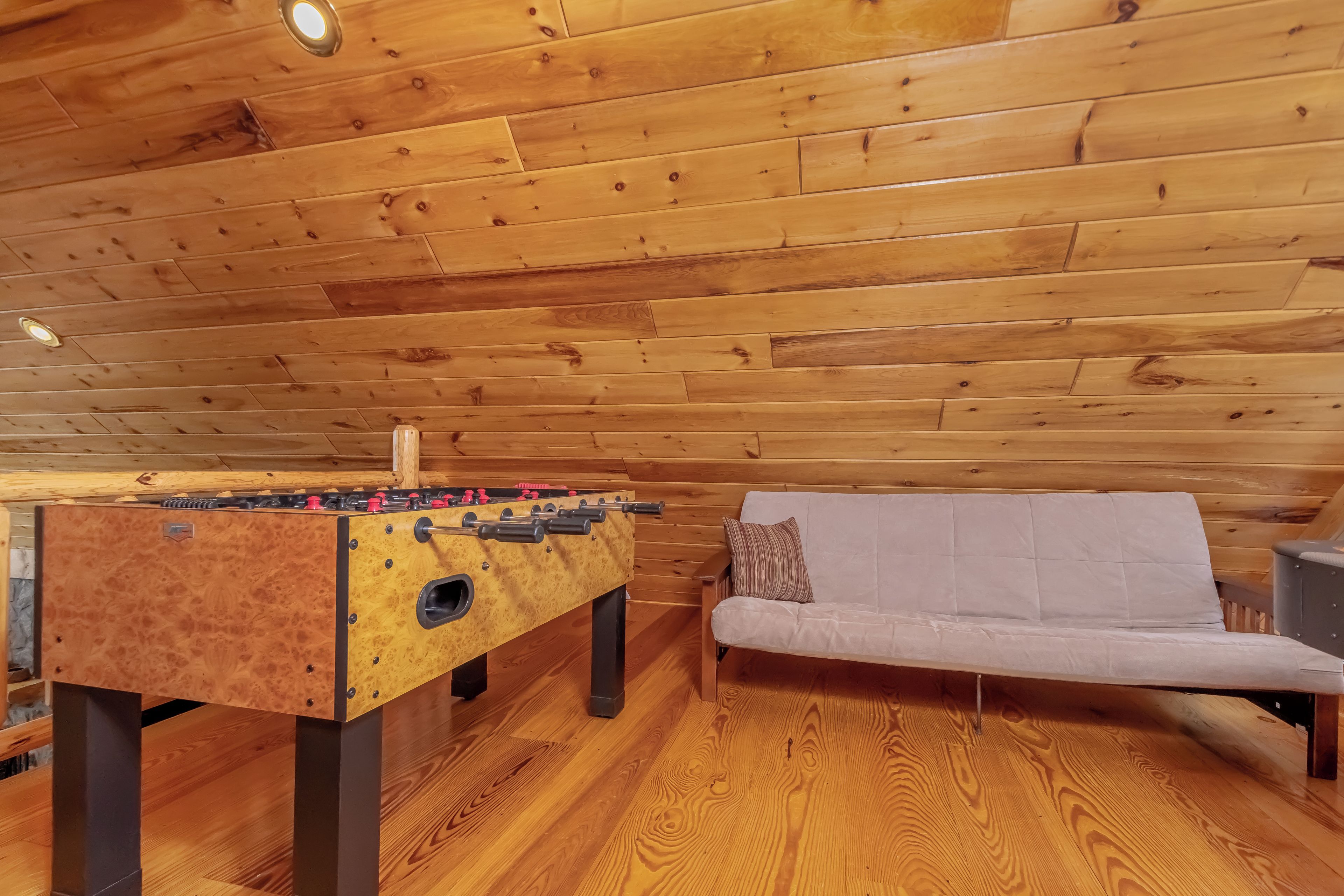 A wooden-floored room with a foosball table and a sofa.