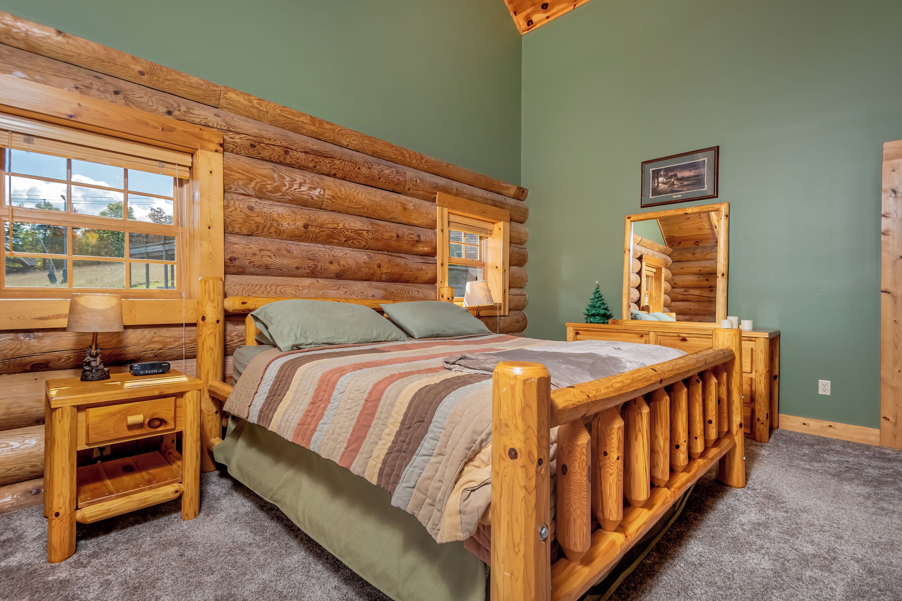 A log cabin bedroom with a wooden bed, a nightstand, a lamp, and a small Christmas tree.