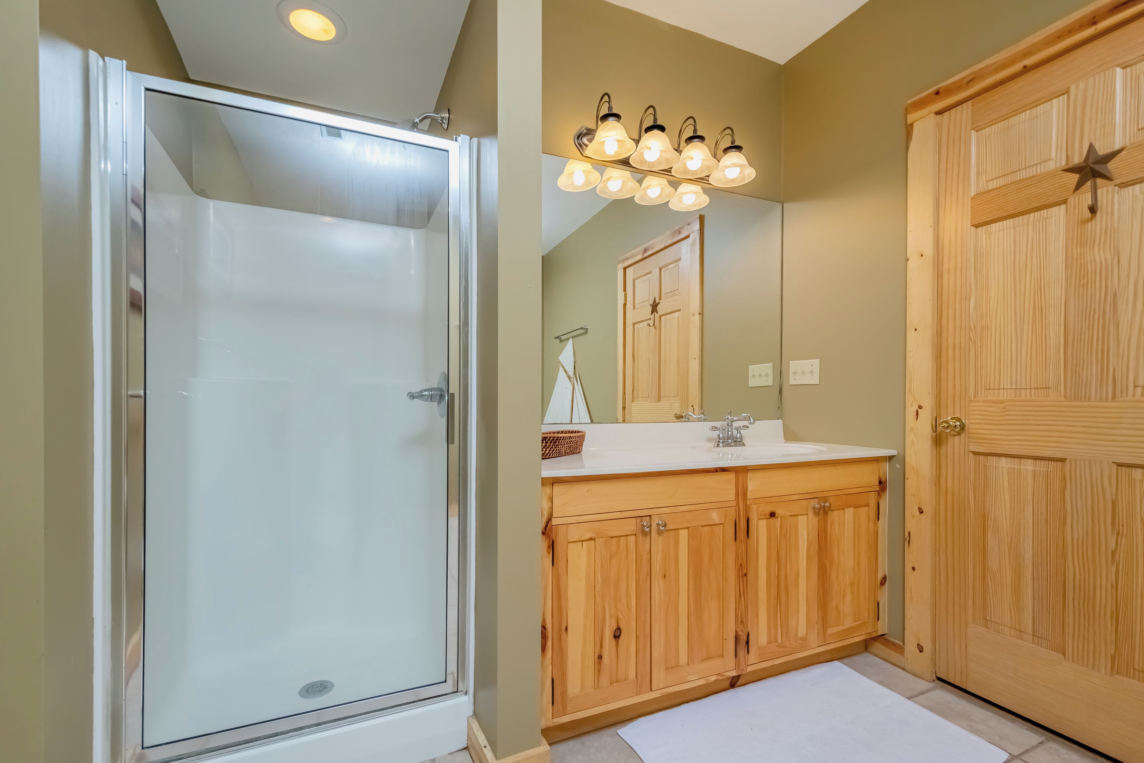 A bathroom with a glass-enclosed shower, wooden cabinets, a sink with a mirror, and a wooden door.