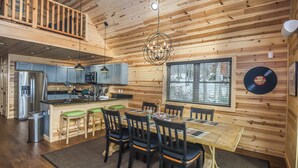 A wooden cabin interior with a dining area, kitchen, and a balcony. - Woods-stock by Taylor Made Deep Creek (McHenry)