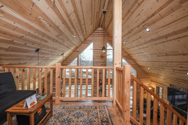 A wooden interior with a high ceiling, a staircase, and a view through large windows. - Woods-stock by Taylor Made Deep Creek (McHenry)