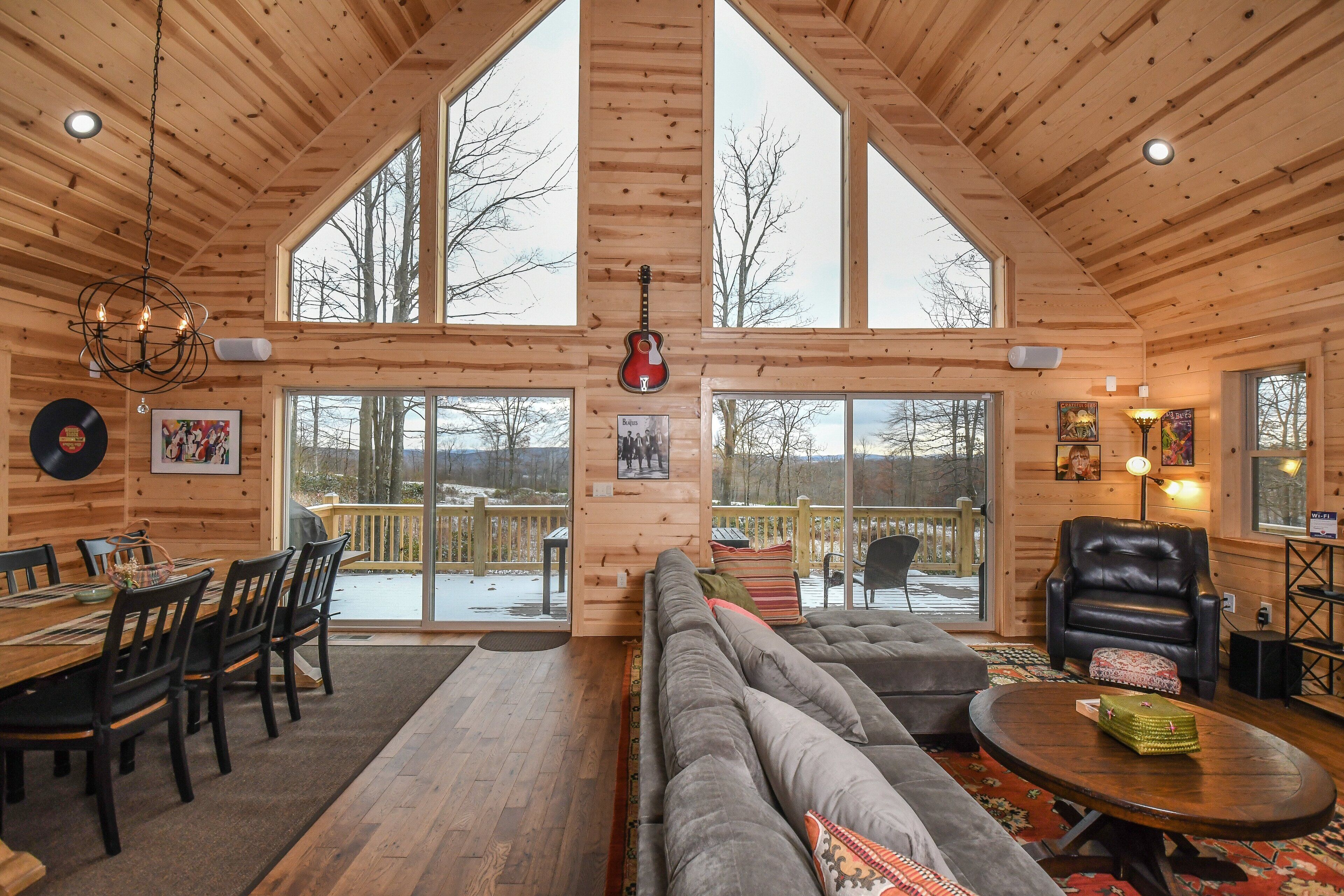 A log cabin interior with a dining area, a large sofa, a leather armchair, and a view through the windows.
