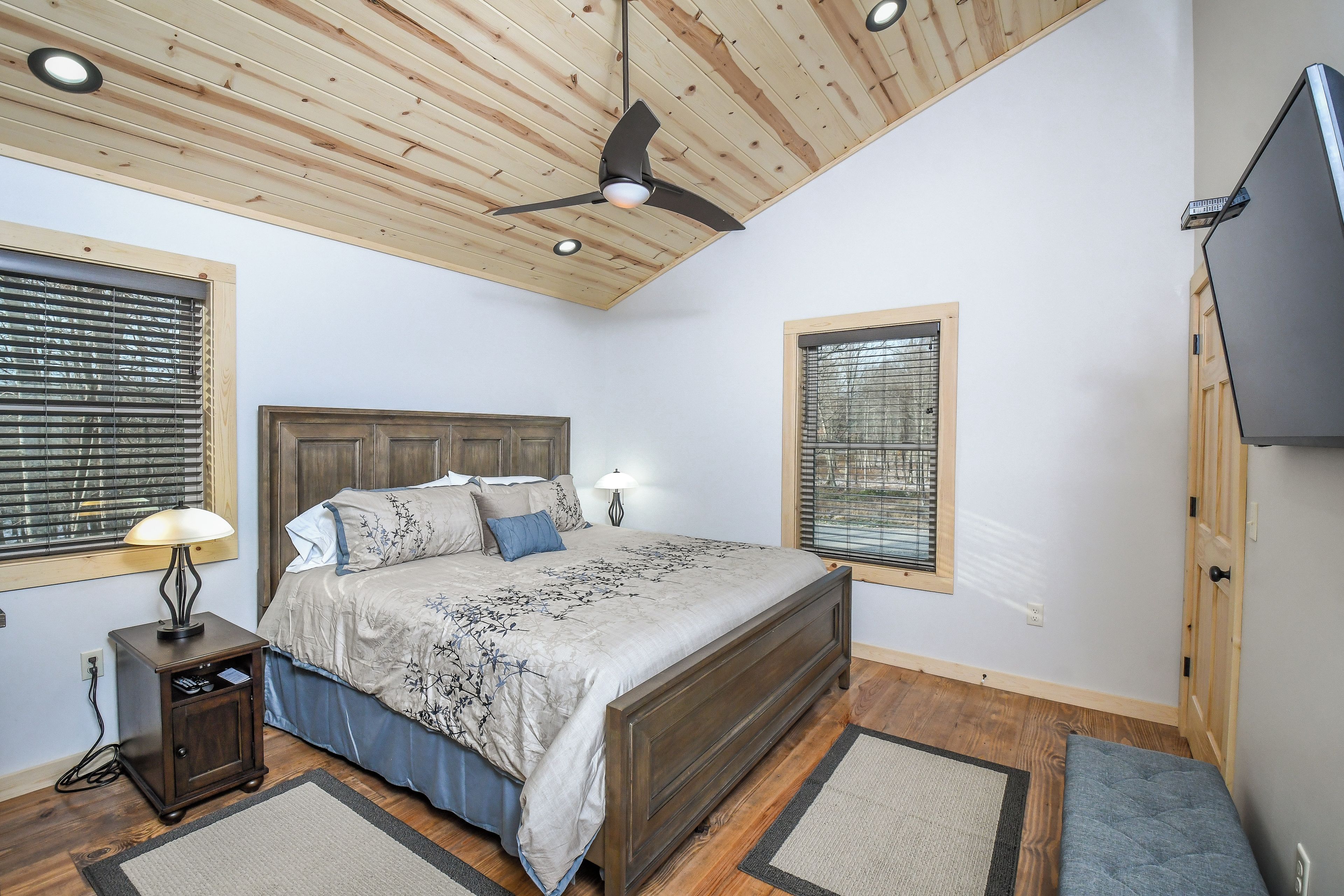 Una camera da letto con soffitto in legno, un letto con copriletto floreale, un comodino con lampada e una TV a parete.