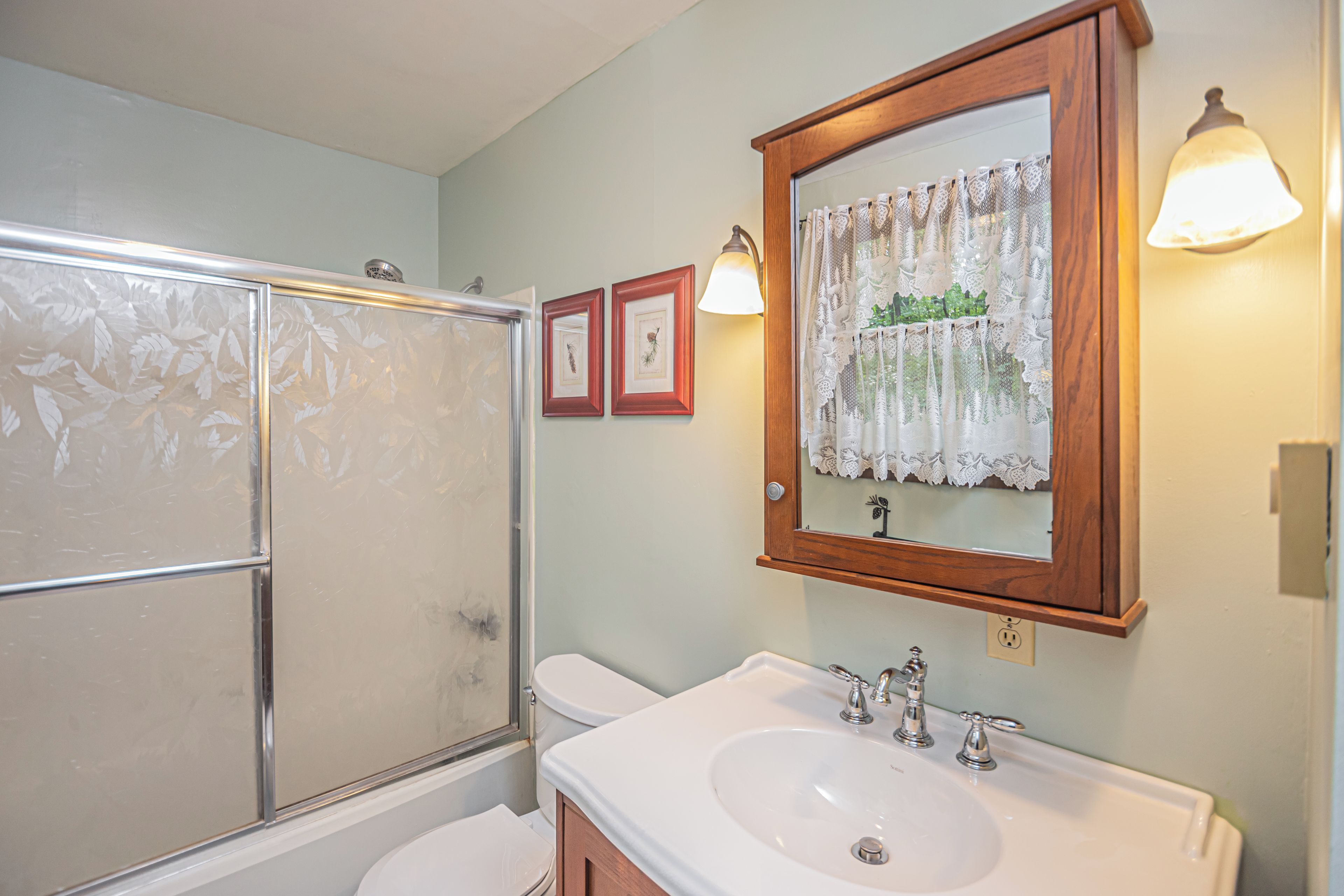A bathroom with a glass shower enclosure, a white sink, and a mirror with a wooden frame.