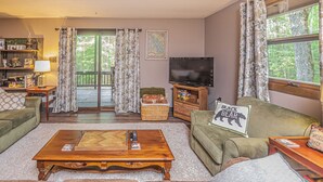 A cozy living room with a green sofa, a wooden coffee table, and a television. - Woodside Retreat by Taylor Made Deep Creek (McHenry)