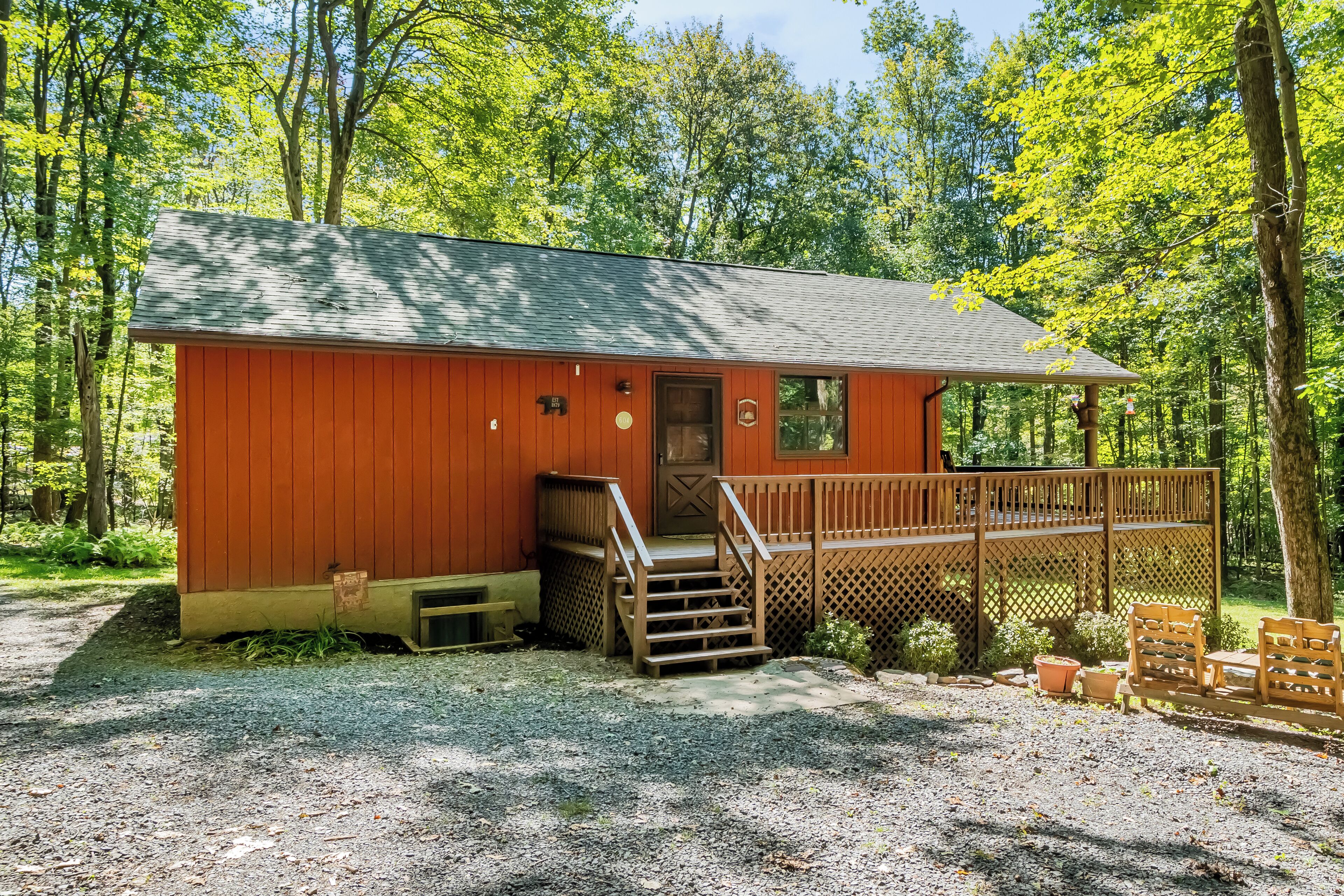 A small, single-story cabin with a wooden deck and a front door, surrounded by trees.