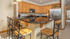 A kitchen with wooden cabinets, stainless steel appliances, and a central island with bar stools. - Bet Your Ace by Taylor Made Deep Creek (McHenry)