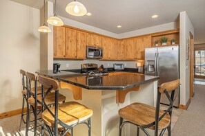 A kitchen with wooden cabinets, stainless steel appliances, and a central island with bar stools. - Bet Your Ace by Taylor Made Deep Creek (McHenry)