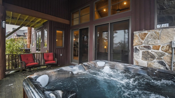 A hot tub on a wooden deck with a stone wall and a view of a house. - Bet Your Ace by Taylor Made Deep Creek (McHenry)