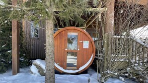 A wooden sauna door with a glass window, surrounded by snow-covered ground and trees. - Bet Your Ace by Taylor Made Deep Creek (McHenry)