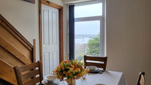 A dining area with a table set for two, a vase of flowers, and a view of a bridge through a window. - Marina Reach, Neyland, Pembrokeshire: Sea views (Neyland)