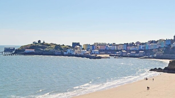 A coastal town with a pier extending into the sea, buildings along the shoreline, and a sandy beach with a few people. - Marina Reach, Neyland, Pembrokeshire: Sea views (Neyland)