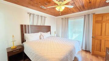 Une chambre avec un plafond en bois, un lit recouvert d’une couette matelassée, une table de chevet avec une lampe et une porte.