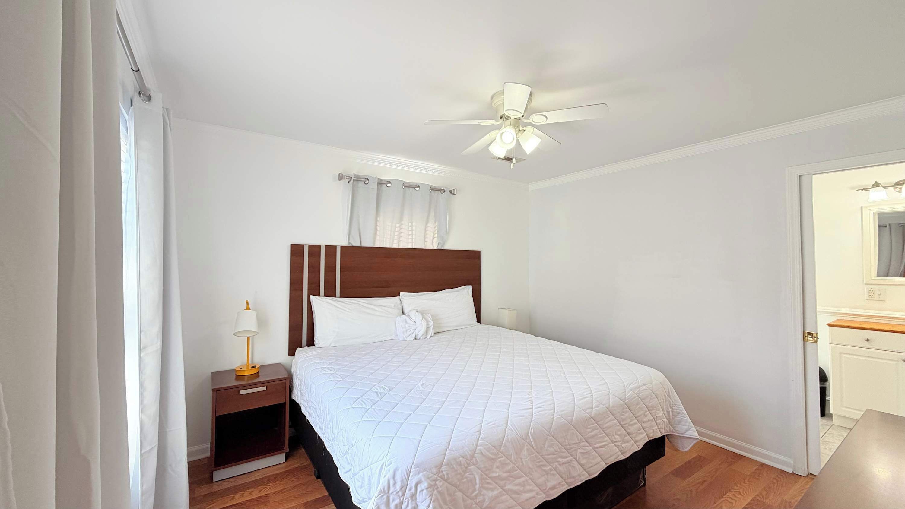 A neatly arranged bedroom with a bed, a nightstand, a ceiling fan, and a door.