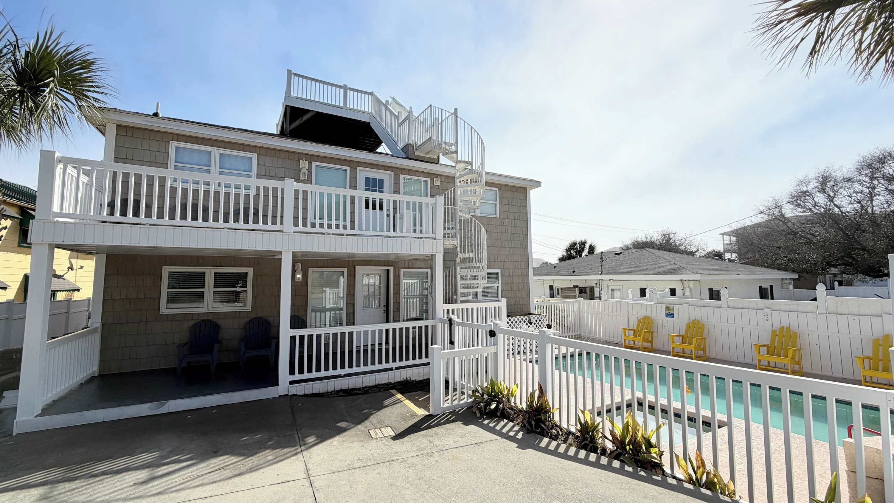 Un bâtiment à deux étages doté d’un balcon, d’une piscine et d’un espace clos avec des chaises jaunes.