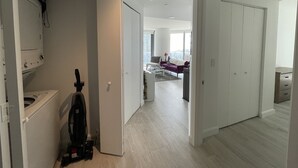 A modern apartment with a laundry area, a living room with a sofa and coffee table, and a view of the city.