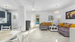 A modern living room with a gray sofa, white dining table, and a kitchen area with dark cabinets and a white refrigerator. - 3 BD Villa with Private pool, Jacuzzi and Volleyball Court (Umag)