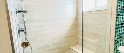 A glass-enclosed shower with a rain showerhead, a handheld showerhead, and a handheld shower attachment. The shower has a mosaic tile floor and a glass door.