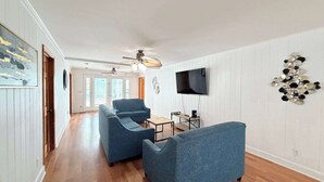 Un salon spacieux doté d’un ventilateur de plafond, d’un téléviseur à écran plat fixé au mur et d’un élément décoratif mural.