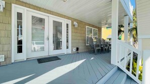 Une véranda avec une terrasse en bois, des rampes blanches et un espace salon avec des chaises.