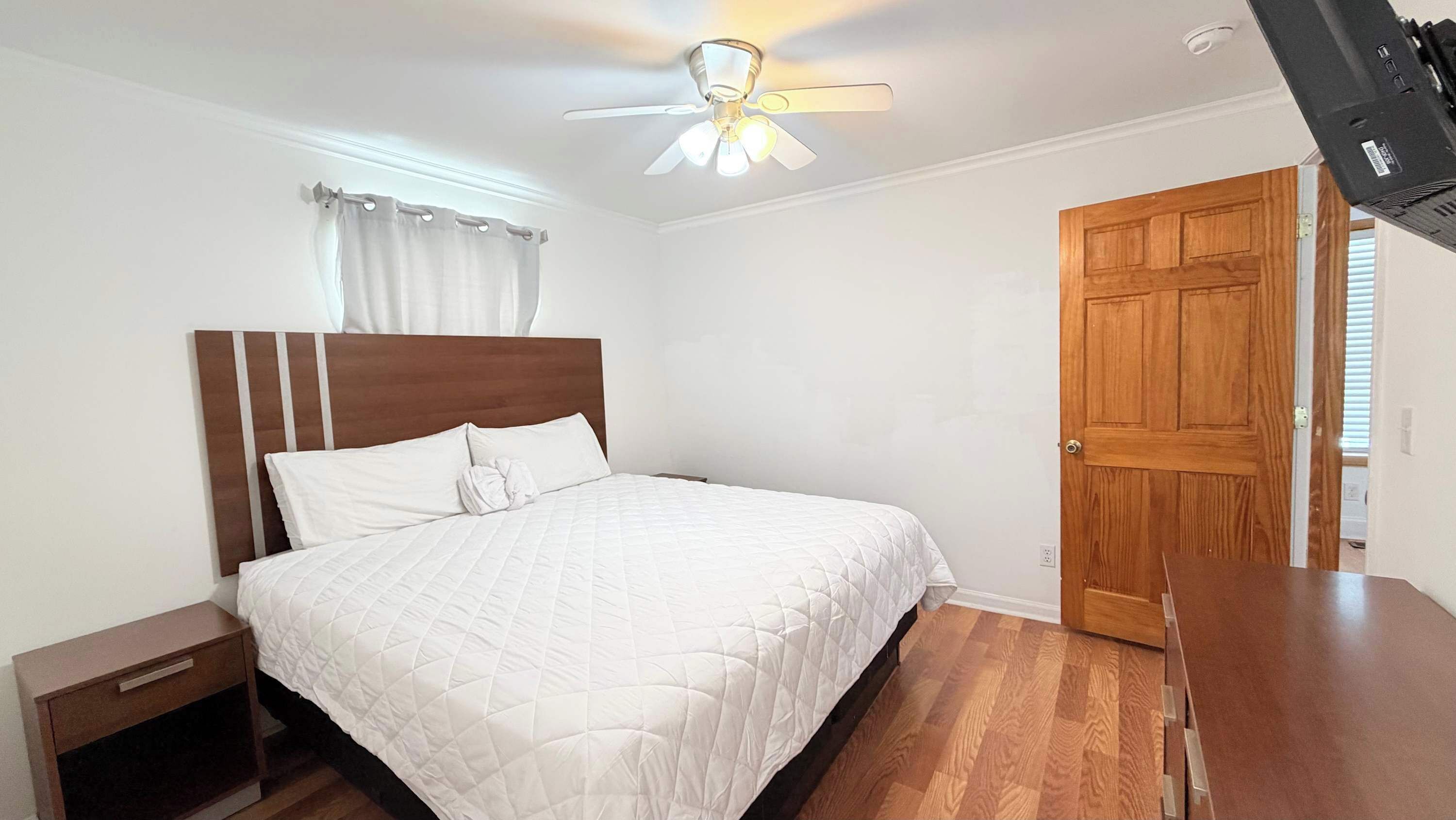 A bedroom with a bed, nightstand, wooden door, and ceiling fan.