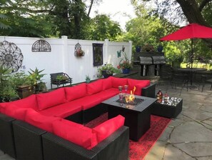 Relax on the patio with a fire feature, surrounded by lush greenery and a barbecue grill.