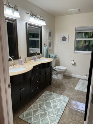 A bathroom with two sinks, a toilet, a window, and a mirror.
