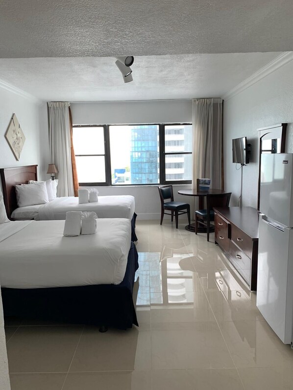A hotel room with two beds, a desk, a chair, a TV, and a refrigerator.
