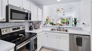 A modern kitchen with white cabinetry, stainless steel appliances, and a large window overlooking a pool. - *NEW 3/2 Pool Home, Private Yard, Great Location! (Jupiter)