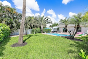 Un patio trasero con piscina, palmeras y una casa con mobiliario exterior.