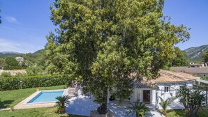 En villa med swimmingpool, omgivet af frodig vegetation og et bjergrigt landskab.