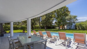 En udendørs terrasse med et glasbord, stole og en pool.