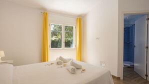 Et hotelværelse med en seng, et vindue med gule gardiner og udsigt til grønne omgivelser.