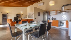Een moderne keuken met een eethoek, met een houten plafond, inbouwapparatuur en oranje kastjes.