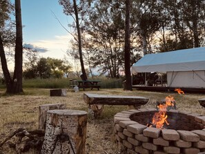 Un terrain de camping équipé d’un foyer, de tables de pique-nique et d’une tente.