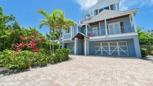 A two-story building with a garage, surrounded by tropical vegetation. - Summer House-8 bedroom, Rooftop, short walk to the beach, private pool/spa and w (Holmes Beach)