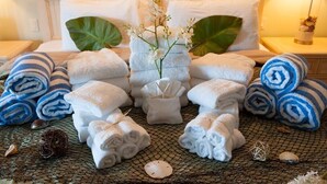 A neatly arranged set of towels and a decorative plant on a bed with a headboard, surrounded by a woven mat and some decorative items. - Summer House-8 bedroom, Rooftop, short walk to the beach, private pool/spa and w (Holmes Beach)