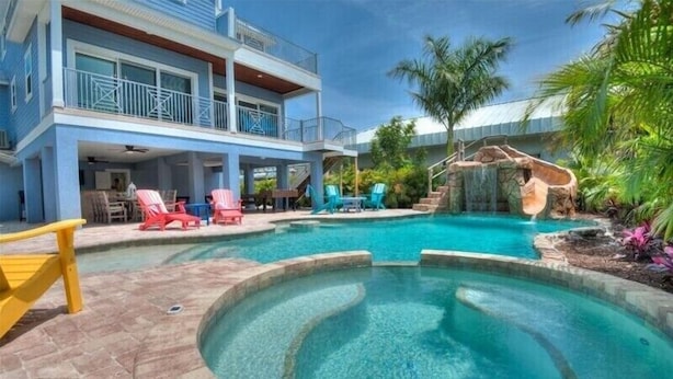 A swimming pool with a waterfall feature, lounge chairs, and a two-story building with balconies. - Summer House-8 bedroom, Rooftop, short walk to the beach, private pool/spa and w (Holmes Beach)
