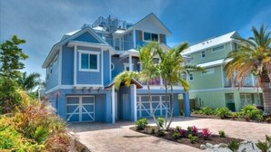 A two-story house with a garage, surrounded by tropical plants and palm trees. - Summer House-8 bedroom, Rooftop, short walk to the beach, private pool/spa and w (Holmes Beach)
