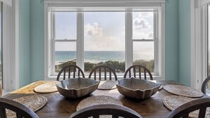 A dining area with a view of the ocean, featuring a wooden table with woven placemats and metal bowls.