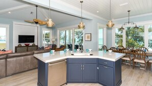 A modern kitchen with a large island, pendant lighting, and a dining area with wooden chairs.