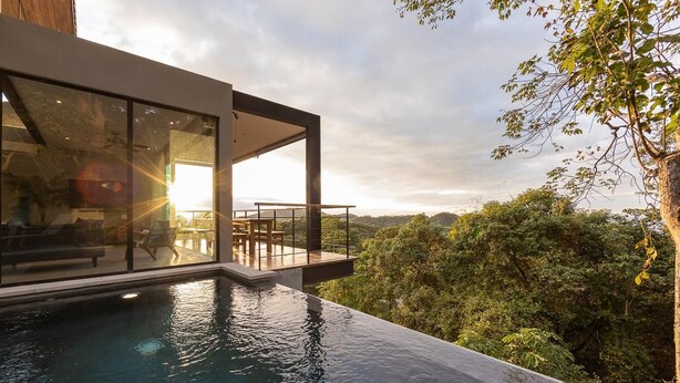 A modern outdoor pool area with a glass enclosure, overlooking a lush forest.