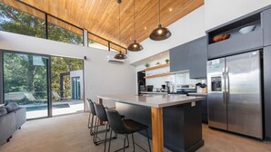 A modern kitchen with a large island, bar stools, and a stainless steel refrigerator.