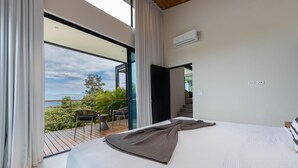 A bedroom with a large bed, a view of the outdoors, and a balcony with chairs.