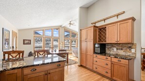 A spacious kitchen with wooden cabinets, granite countertops, and large windows offering views of a snowy landscape. - Lily Mountain Lodge - Amazing Mountains Views, Private Hot Tub, Great Location (Estes Park)