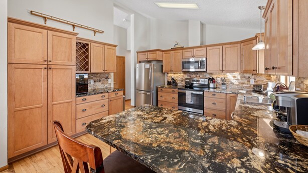 A kitchen with wooden cabinets, granite countertops, stainless steel appliances, and a large island. - Lily Mountain Lodge - Amazing Mountains Views, Private Hot Tub, Great Location (Estes Park)
